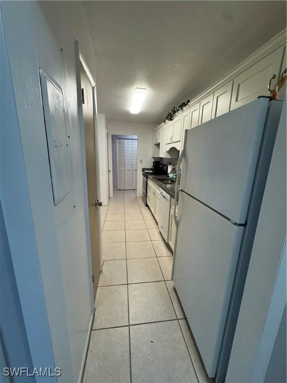 kitchen featuring light tile patterned floors, black electric range oven, stainless steel dishwasher, dark countertops, and freestanding refrigerator