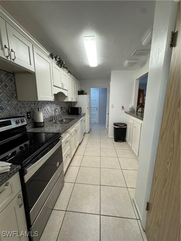 kitchen with light tile patterned floors, backsplash, a sink, stainless steel range with electric stovetop, and dishwashing machine