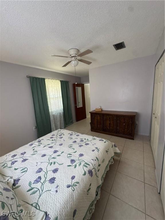 bedroom with light tile patterned flooring, visible vents, ceiling fan, and a textured ceiling