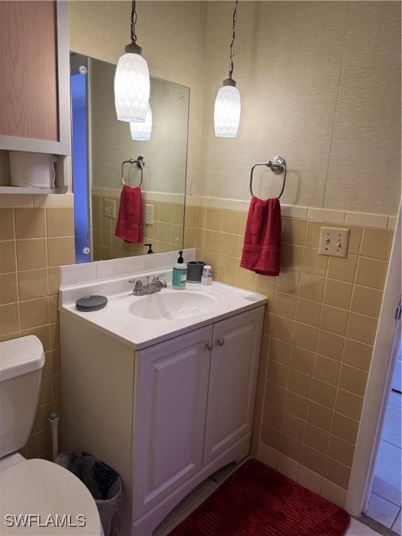 bathroom featuring toilet, vanity, wainscoting, and tile walls