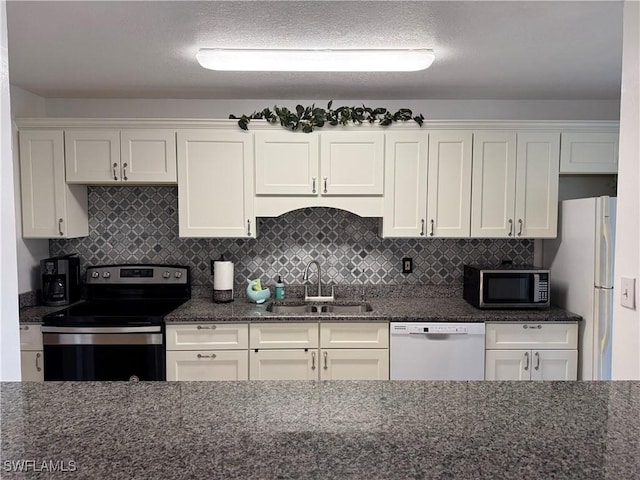 kitchen with dark stone counters, a sink, stainless steel appliances, tasteful backsplash, and white cabinetry