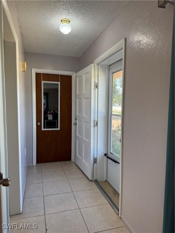 doorway with a textured ceiling, a healthy amount of sunlight, and light tile patterned flooring