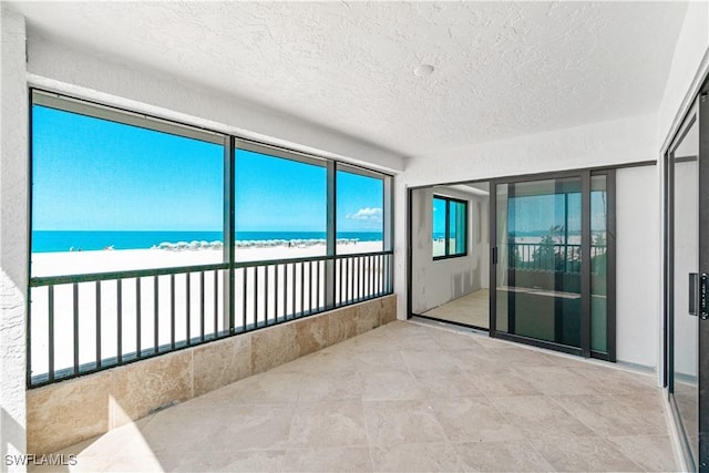 26130 Hickory Blvd Unit 1B, Bonita Springs, FL 34134 - unfurnished sunroom with a textured ceiling, view of water and beach, and tile patterned floors