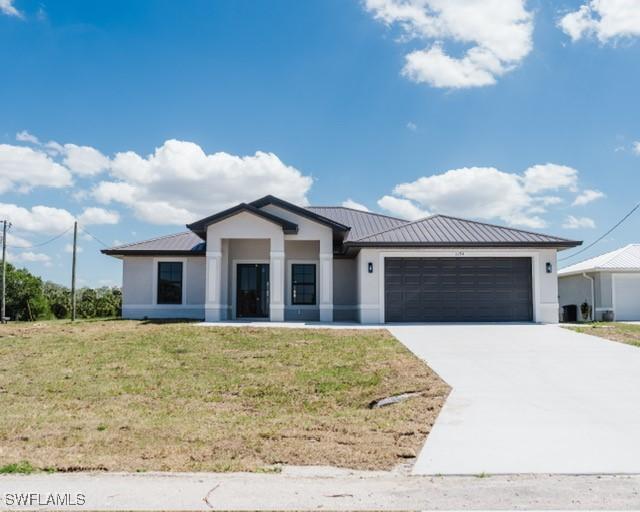 1194 Calico St, Labelle, FL 33935 - view of front of property featuring concrete driveway, a front lawn, metal roof, and a garage