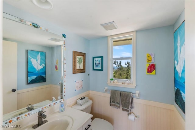 bathroom featuring toilet, visible vents, wainscoting, and vanity