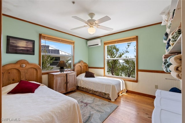bedroom with light wood-style floors, a wall mounted air conditioner, wainscoting, and multiple windows