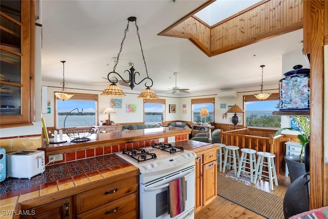 kitchen with gas range gas stove, open floor plan, an AC wall unit, tile countertops, and light wood-type flooring