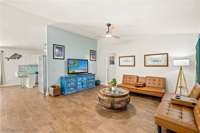 living area with vaulted ceiling, light wood finished floors, baseboards, a ceiling fan, and a textured ceiling