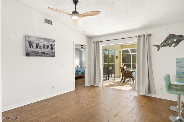 spare room featuring ceiling fan, visible vents, baseboards, a textured ceiling, and wood finished floors
