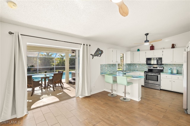 kitchen featuring electric stove, tasteful backsplash, black microwave, a ceiling fan, and a peninsula