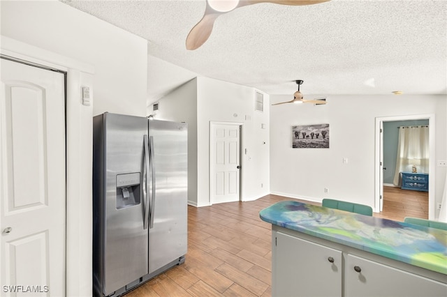 kitchen with stainless steel refrigerator with ice dispenser, a ceiling fan, light wood finished floors, and a textured ceiling
