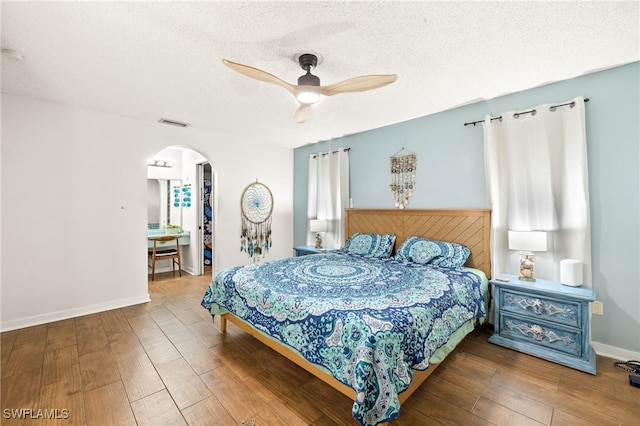 bedroom with visible vents, arched walkways, a textured ceiling, and wood finished floors