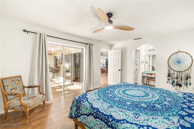 bedroom with arched walkways, wood finished floors, access to outside, visible vents, and a textured ceiling