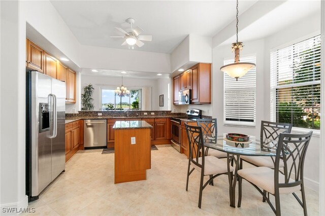 kitchen with brown cabinets, hanging light fixtures, appliances with stainless steel finishes, ceiling fan with notable chandelier, and a kitchen island