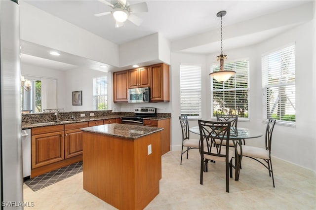 kitchen featuring appliances with stainless steel finishes, a sink, brown cabinetry, plenty of natural light, and a kitchen island
