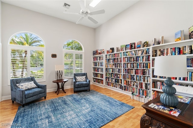 living area featuring wall of books, ceiling fan, wood finished floors, and visible vents