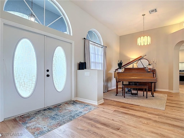 foyer entrance with visible vents, a chandelier, baseboards, arched walkways, and wood finished floors