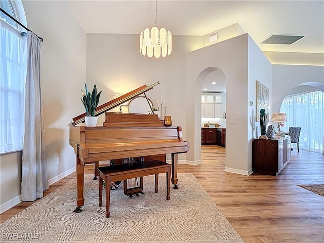 living area featuring visible vents, light wood-style floors, a chandelier, and arched walkways