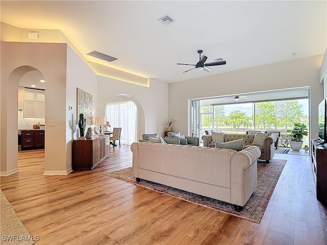 living room featuring arched walkways, visible vents, ceiling fan, and light wood-style floors