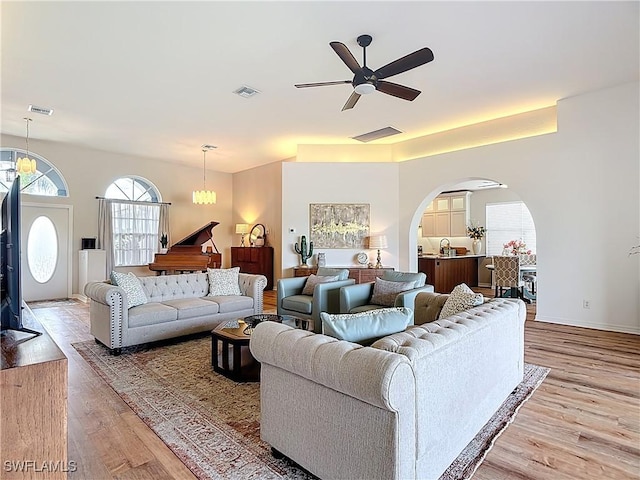 living area with arched walkways, visible vents, ceiling fan, and light wood-style flooring