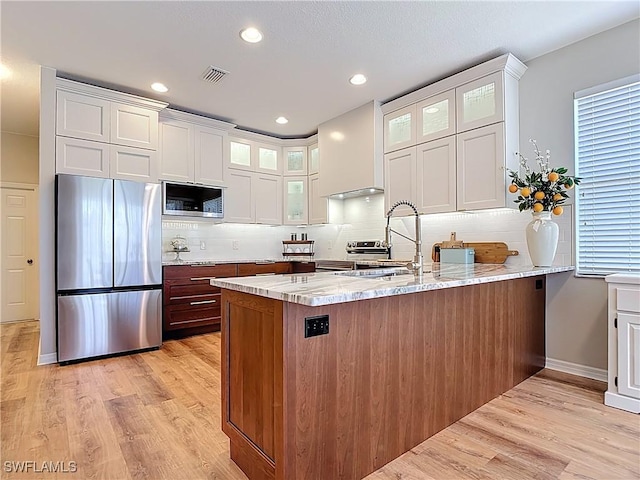 kitchen featuring light stone counters, appliances with stainless steel finishes, light wood finished floors, a sink, and a peninsula