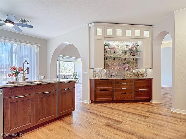 bar featuring a sink, ceiling fan, light wood-type flooring, and arched walkways