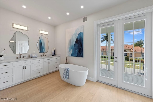bathroom with double vanity, a soaking tub, wood finished floors, recessed lighting, and baseboards