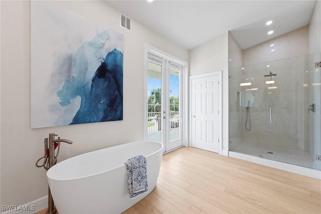 bathroom featuring french doors, a shower stall, wood finished floors, a soaking tub, and recessed lighting