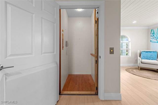 hall with baseboards, elevator, wood finished floors, and ornamental molding