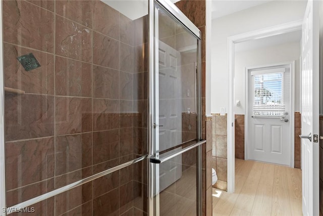 bathroom with a shower stall, wood finished floors, tile walls, wainscoting, and toilet