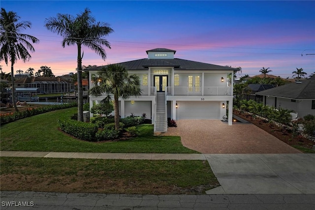 coastal inspired home with french doors, stairs, decorative driveway, a garage, and a front lawn