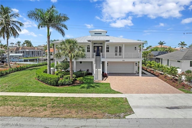 coastal inspired home featuring stairway, decorative driveway, a garage, a front yard, and a standing seam roof