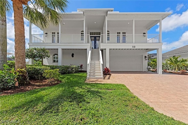 coastal inspired home featuring french doors, stairway, decorative driveway, a garage, and a front lawn