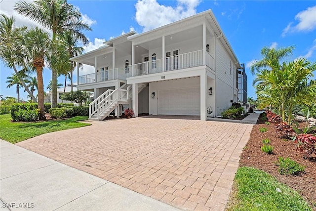 raised beach house featuring decorative driveway, stairs, a garage, and a porch