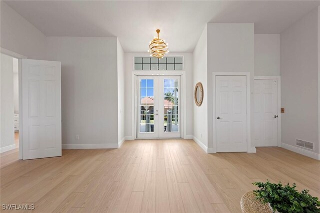 entrance foyer featuring french doors, light wood finished floors, a chandelier, and baseboards