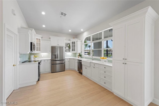 kitchen featuring stainless steel appliances, light wood-style flooring, a sink, glass insert cabinets, and white cabinetry