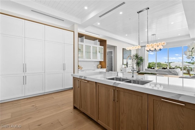 201 8th St S Unit 301, Naples, FL 34102 - kitchen with light stone counters, a sink, white cabinetry, beamed ceiling, and light wood-style floors