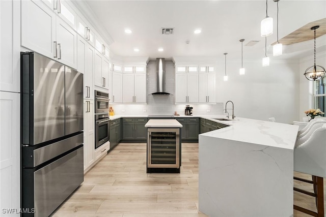 kitchen featuring a sink, a peninsula, beverage cooler, stainless steel appliances, and wall chimney exhaust hood