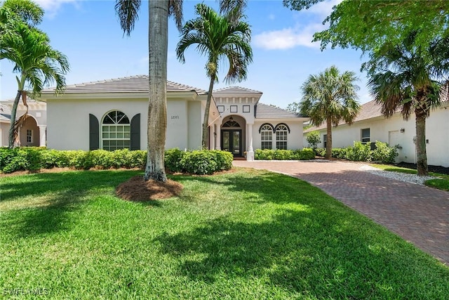 mediterranean / spanish house featuring decorative driveway, french doors, a front yard, and stucco siding