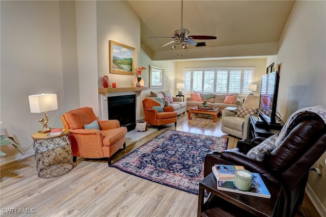 living area featuring vaulted ceiling, a ceiling fan, wood finished floors, a fireplace with flush hearth, and baseboards