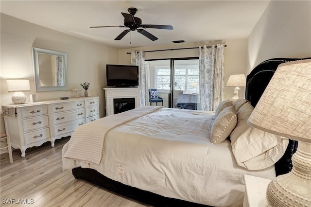 bedroom featuring a ceiling fan, a glass covered fireplace, visible vents, and light wood-type flooring