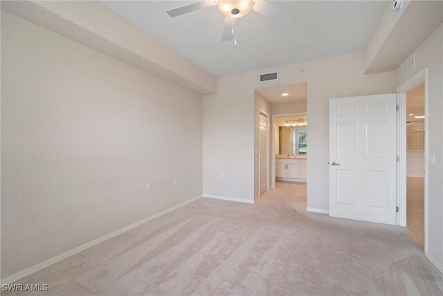 unfurnished bedroom featuring light carpet, ensuite bathroom, visible vents, and baseboards