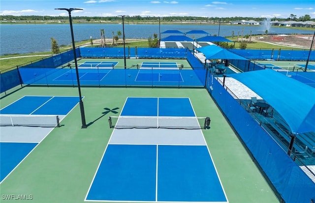 view of tennis court with a water view and fence