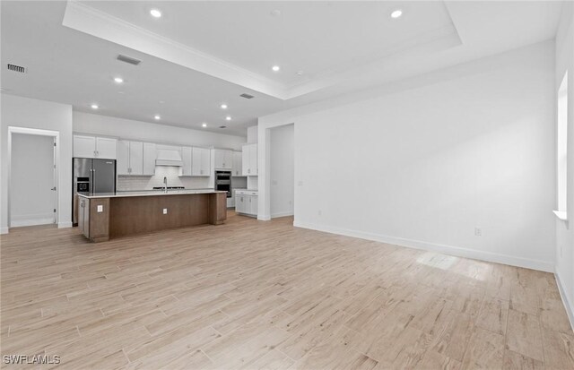 kitchen with appliances with stainless steel finishes, light wood-style floors, white cabinetry, open floor plan, and a tray ceiling