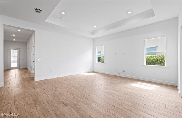 empty room with visible vents, ornamental molding, baseboards, a tray ceiling, and light wood-style flooring