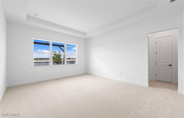 unfurnished room with baseboards, a tray ceiling, and light carpet
