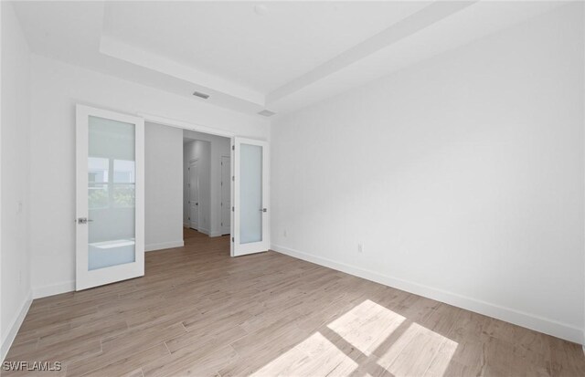 empty room with baseboards, visible vents, light wood-style flooring, and a raised ceiling