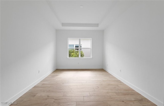 spare room featuring baseboards, light wood finished floors, and a tray ceiling