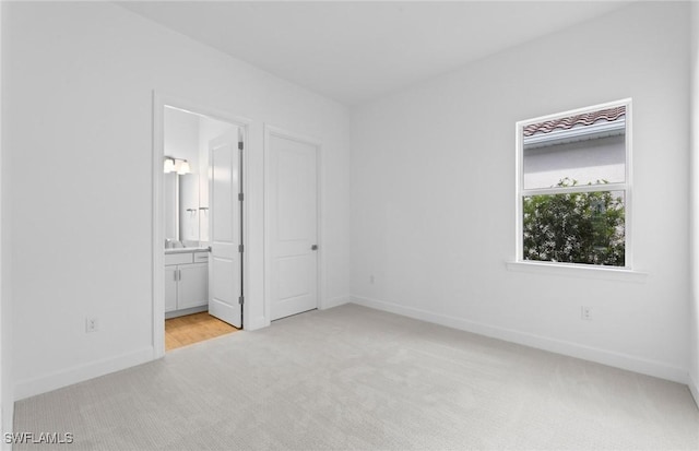 unfurnished bedroom with baseboards, ensuite bath, and light carpet