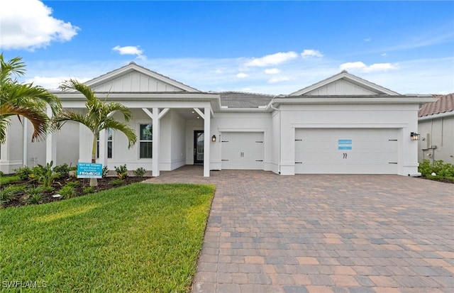 single story home featuring board and batten siding, a front yard, a garage, decorative driveway, and stucco siding